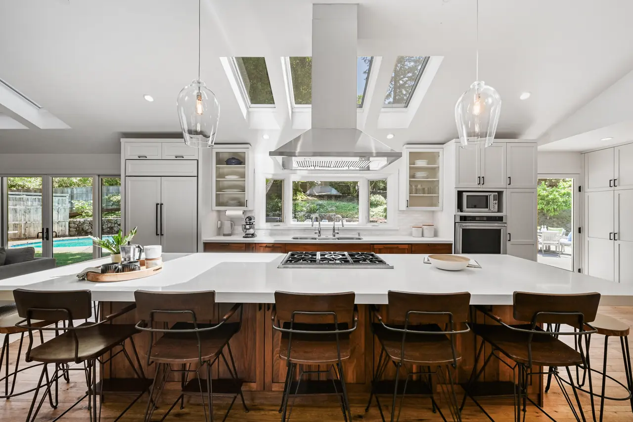 Kitchen under skylights, with a long island, a cooktop and a row of wood stools